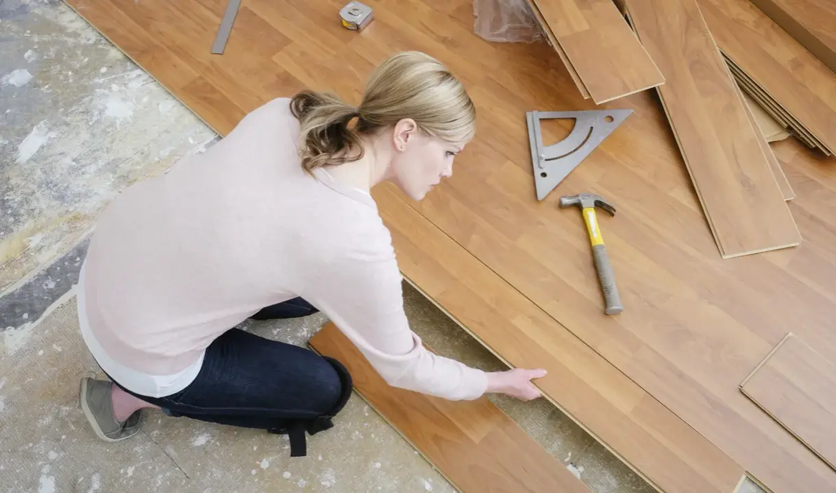 Frau verlegt Laminat, achtet auf die Ausrichtung. Werkzeug liegt bereit. Vermeiden Sie Fehler beim Laminat verlegen.