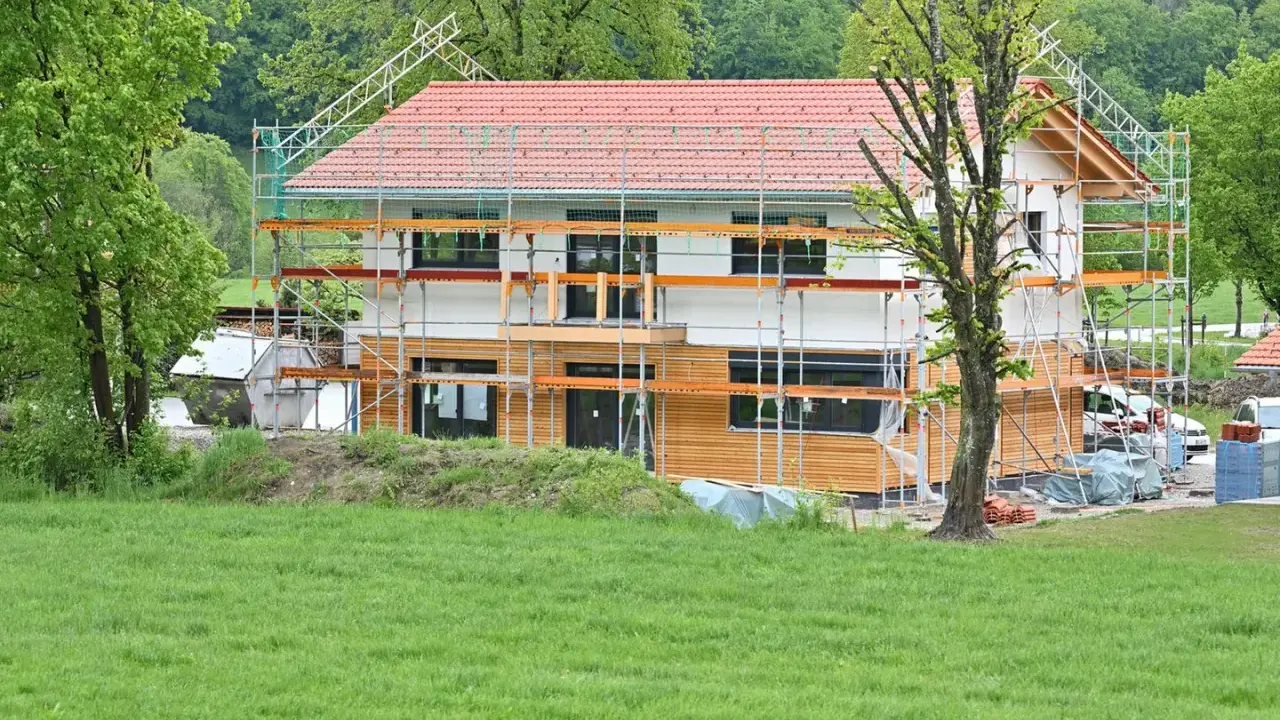Ein Haus im Bau, umgeben von Gerüsten. Man sieht, wie man ein Haus baut, mit Holzfassade und rotem Ziegeldach.