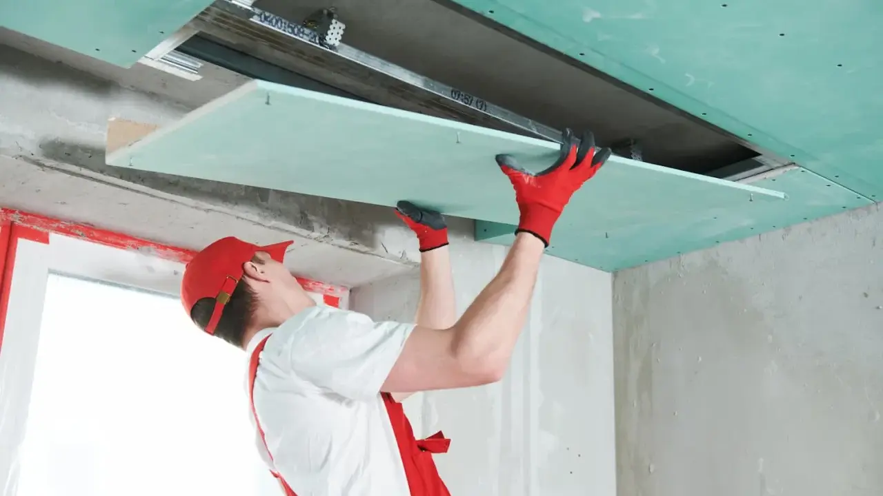 Handwerker mit roten Handschuhen montiert Gipskartonplatten an der Decke, um das Zimmer zu isolieren.