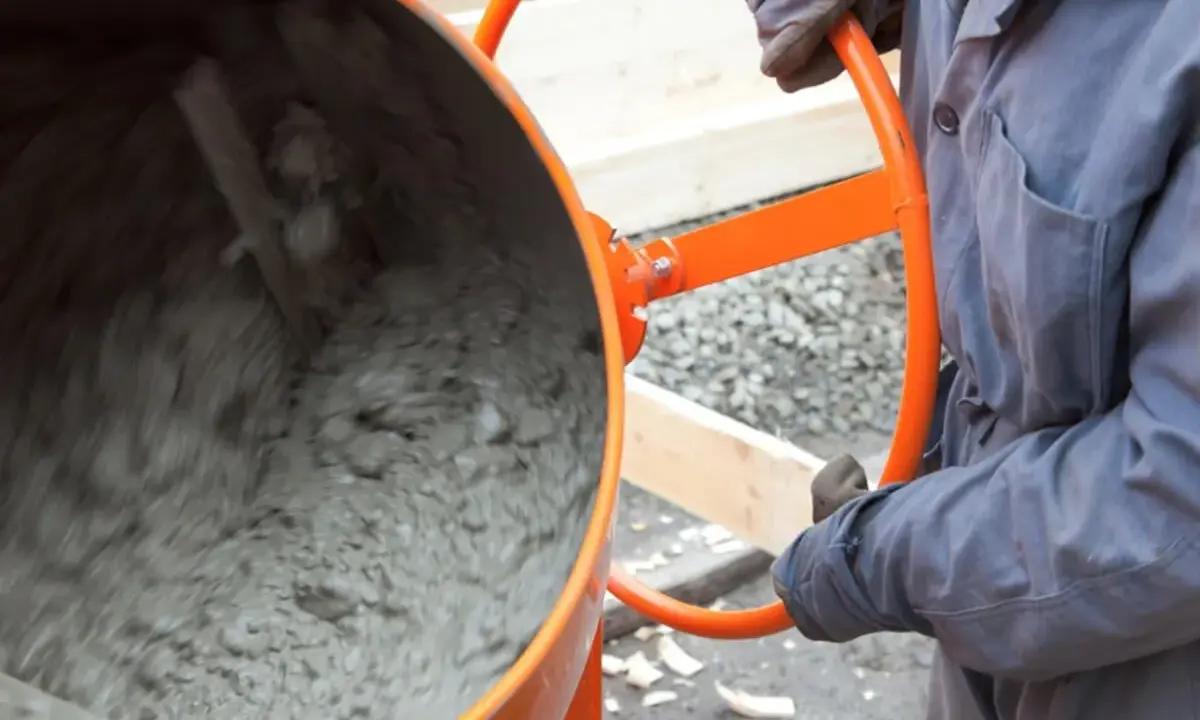 Person in Arbeitskleidung bedient eine Betonmischmaschine, um Beton zu mischen.