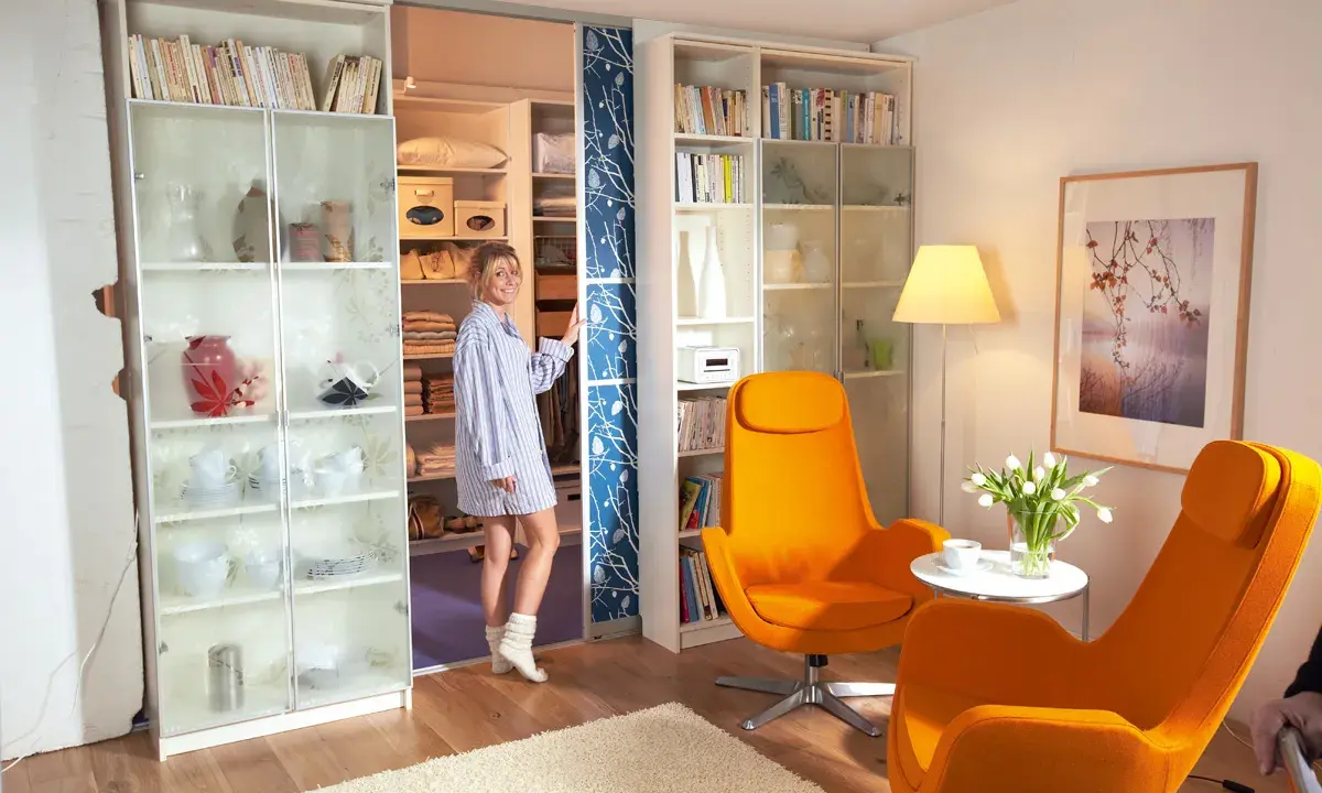 Frau steht vor einem begehbaren Kleiderschrank, den sie selber machen könnte. Links ein Regal mit Geschirr, rechts ein Regal mit Büchern.