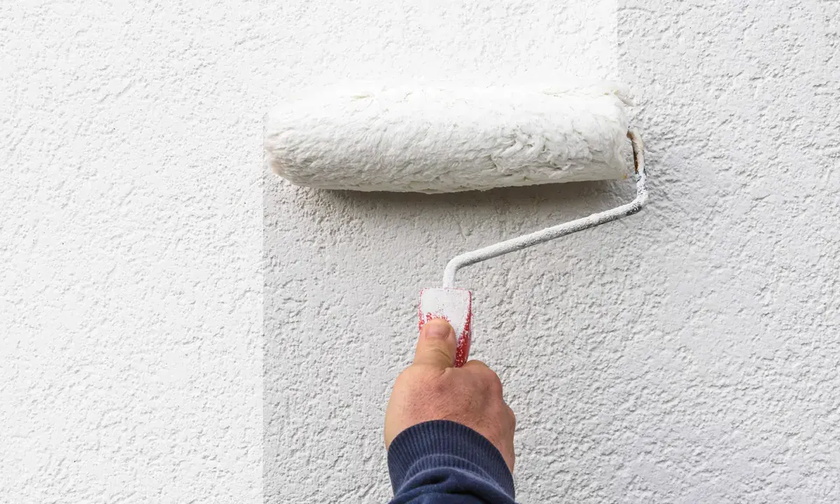 Hand rollt weiße Farbe auf eine strukturierte Wand. Man sieht, welche Wandfarbe am besten deckt.