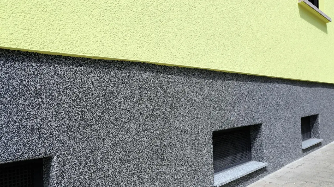 Der Sockel ist mit einem robusten, grauen Körnchenputz verputzt, der gut zu den kleinen Kellerfenstern passt.