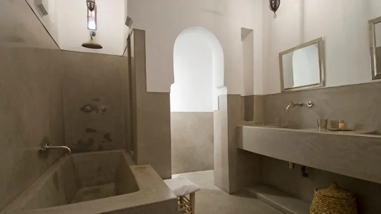 Modernes Badezimmer mit einer freistehenden Badewanne und einem Waschbecken aus Tadelakt. Ein großer Spiegel und ein traditioneller Korb vervollständigen den Look.