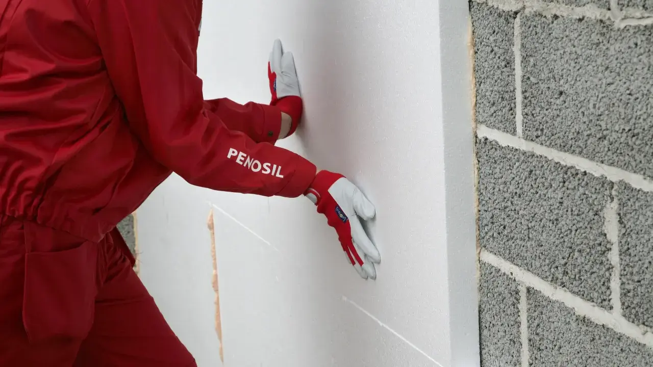 Hand mit Handschuh drückt WDVS Schaum an eine Betonwand.