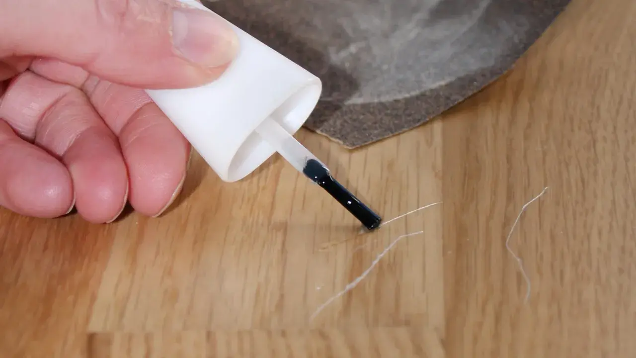 Mit einem Lackstift und Schleifpapier werden Kratzer auf dem Laminat repariert.