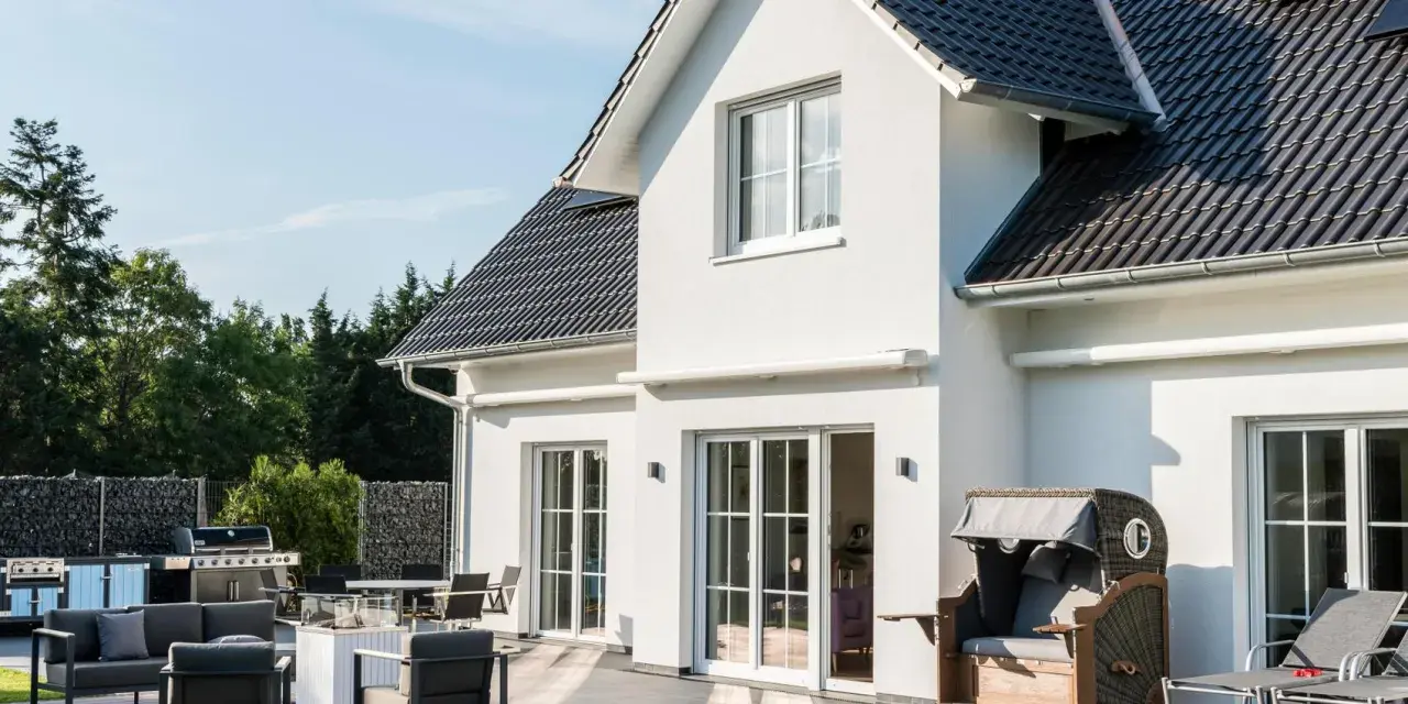 Modernes Haus mit weißen Wänden, dunklem Dach und großer Terrasse. Verschiedene haus stile sind hier vereint, von der Fassade bis zur Gartengestaltung.