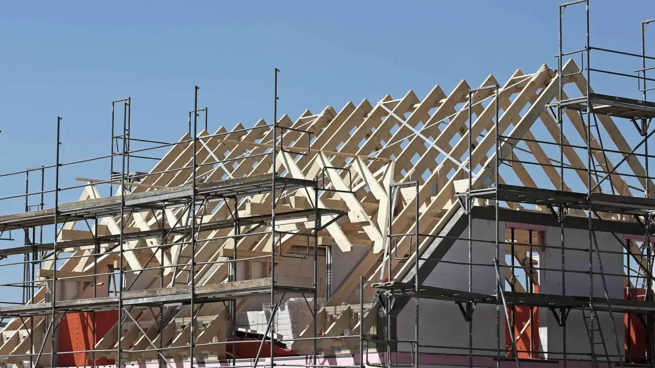 Holzkonstruktion eines Dachstuhls im Bau, umgeben von Gerüsten. Ein Architekt plant den Bau dieses Hauses.