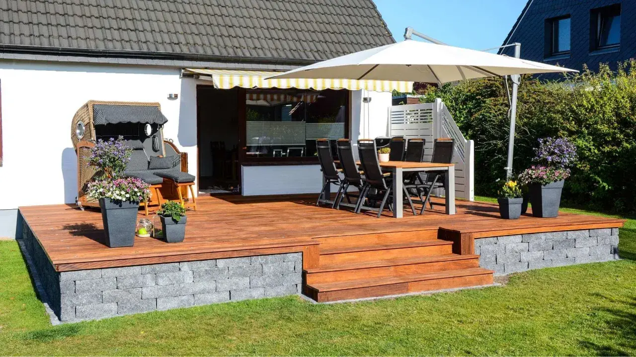 Eine schöne garten terrasse mit Holzdielen, Sitzmöbeln, Sonnenschirm und Blumen. Perfekt für entspannte Stunden im Freien.
