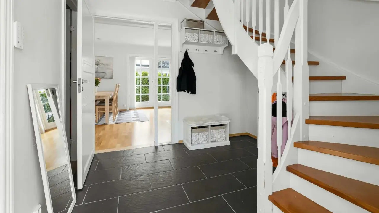 Helle Diele mit dunklem Fliesenboden, Spiegel, Garderobe und einer weißen Treppe, die auf eine **steintreppe renovieren**-Idee hindeutet.
