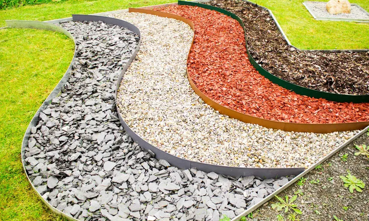 Geschwungene Beete mit verschiedenen Schichten aus grauem Schiefer, hellem Kies, roter Rindenmulch und dunklem Rindenmulch, die durch Metallkanten für rasenkanten setzen getrennt sind.