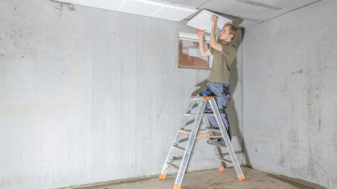 Mann auf Leiter montiert weiße Platten zur kellerdecke isolieren.