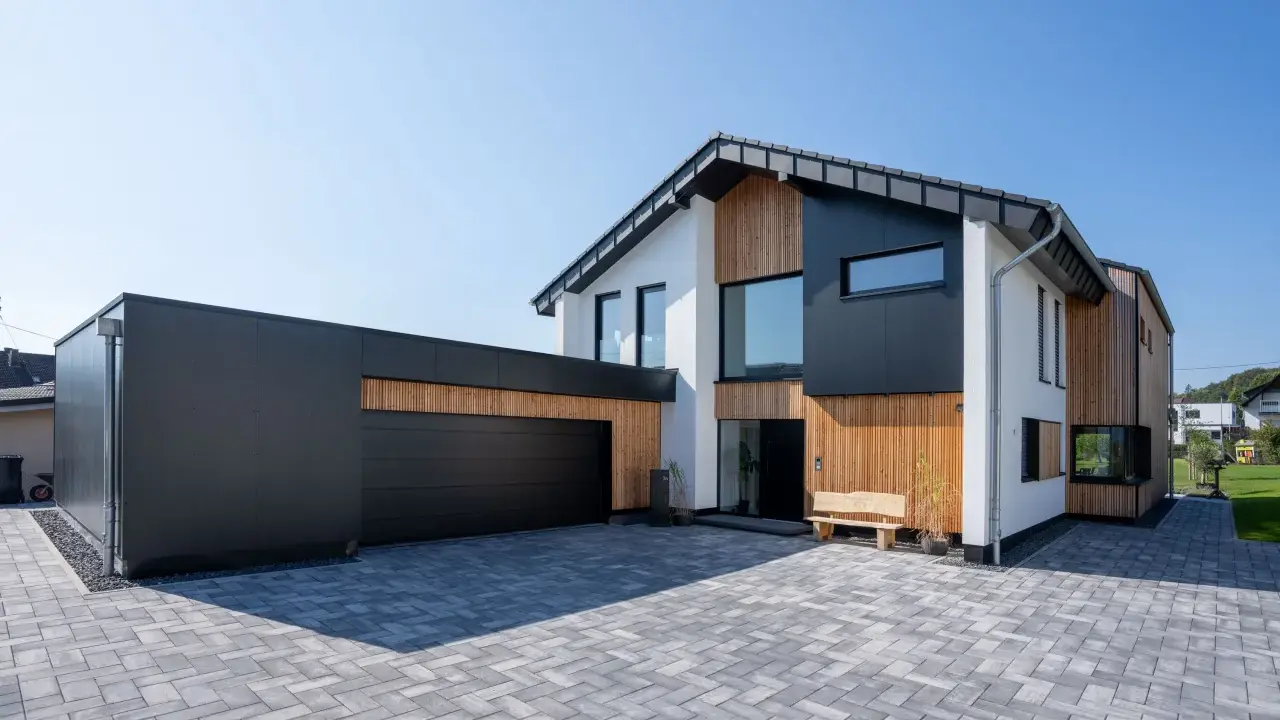 Modernes Haus mit Garage, dessen Satteldach modern interpretiert ist. Holz und dunkle Fassadenelemente prägen das Bild.