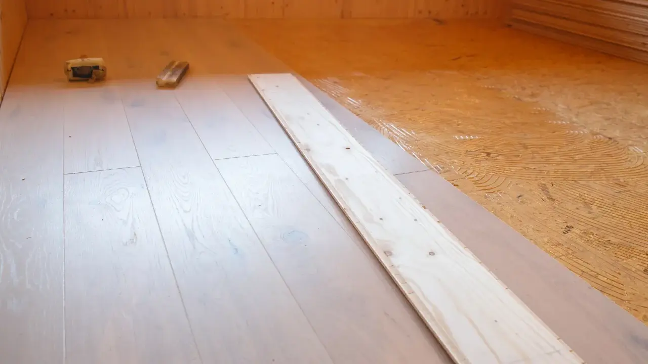 Holzboden wird verlegt. OSB-Platten sind mit Kleber vorbereitet, darauf werden helle Dielen verlegt.