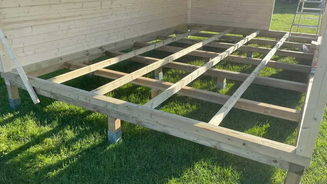 Holzkonstruktion für das Gartenhaus. Der Boden wird auf Balken und Pfosten errichtet, die auf dem Rasen stehen.
