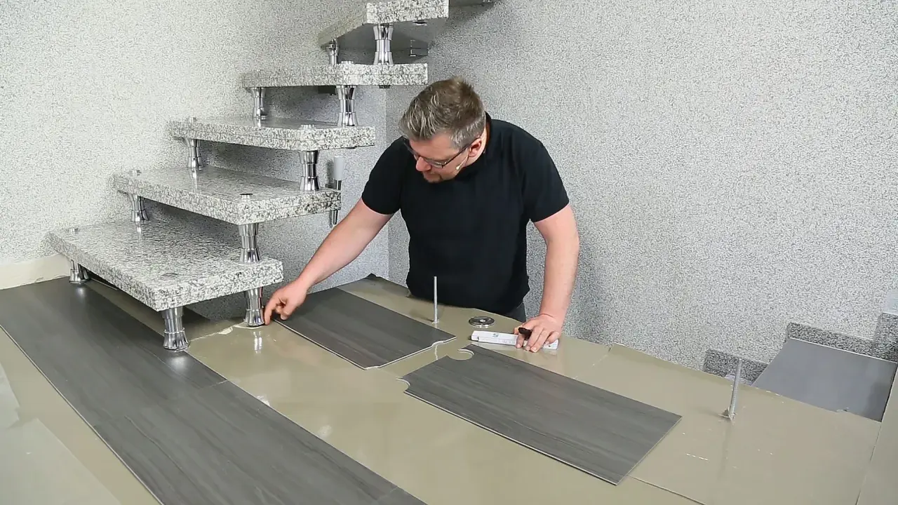 Mann verlegt PVC-Boden. Die grauen Planken werden passgenau zugeschnitten und neben einer modernen Treppe ausgelegt.