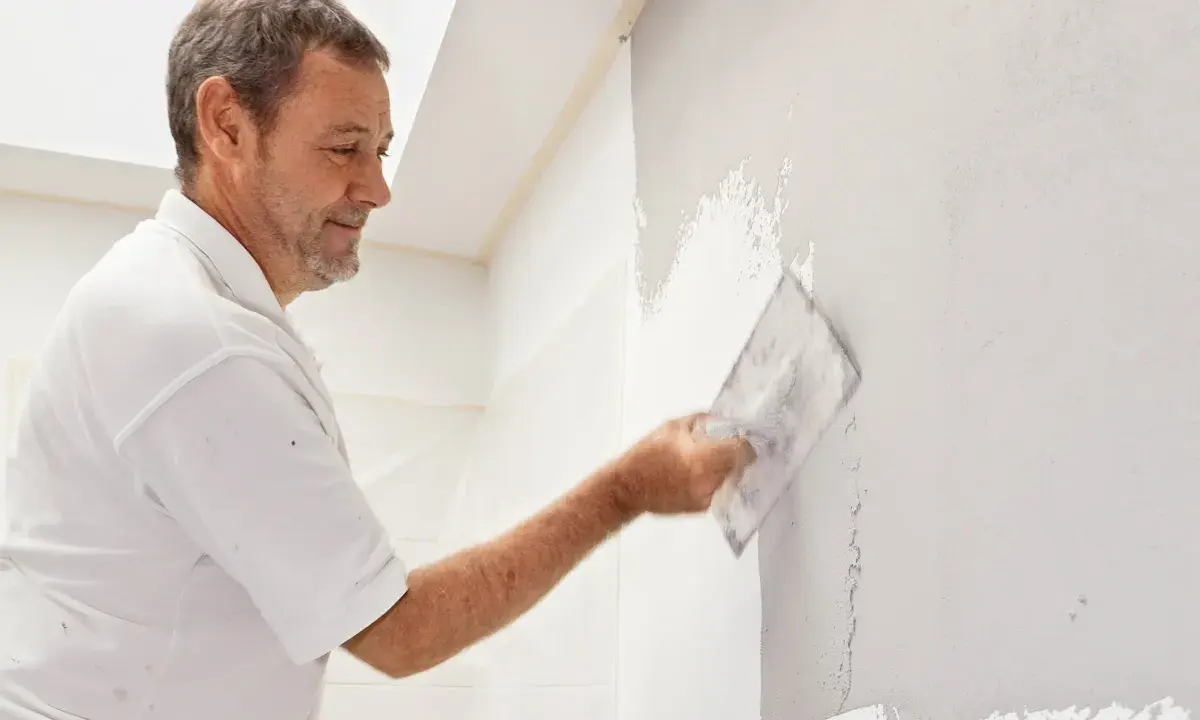 Mann verputzt eine Wand mit einer Kelle. Die Arbeit im Bad ist fast fertig.