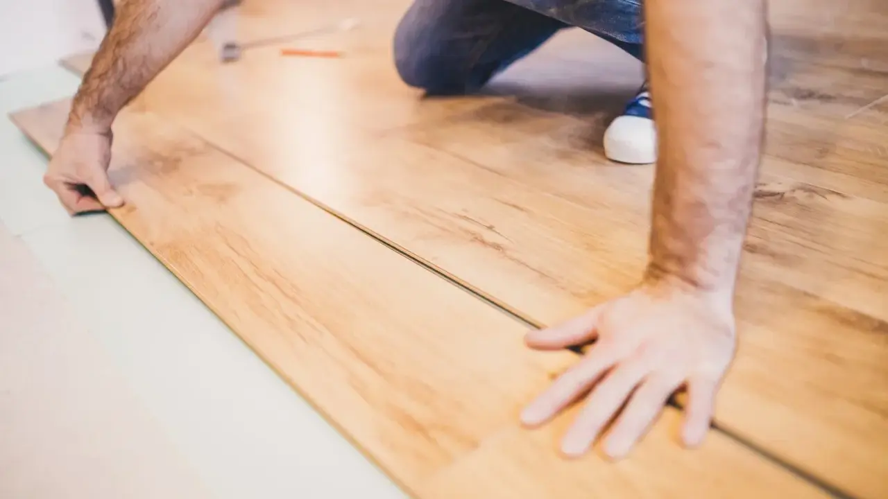 Mann verlegt Laminat. Die Holzoptik der Dielen wird sorgfältig zusammengefügt.