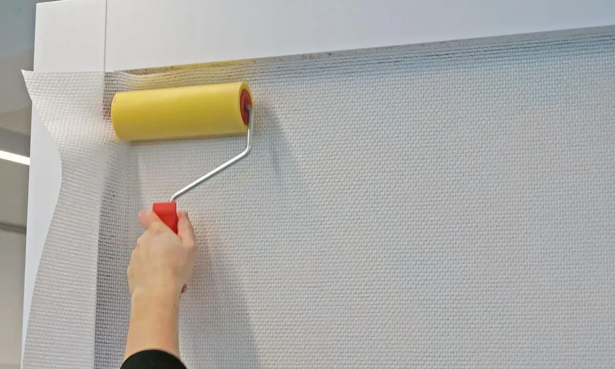 Mit einem gelben Farbroller wird eine weiße Tapete spachteln.