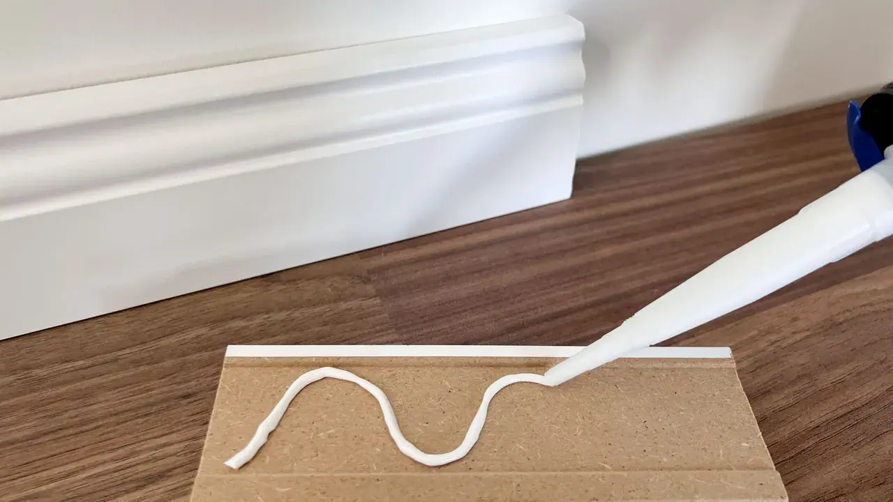 Kleber wird auf eine Sockelleiste aufgetragen, um sie an der Wand zu befestigen.