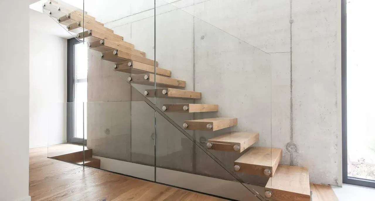 Moderne Holztreppe mit Glasgeländer an Betonwand. Hier können Sie die treppe kosten berechnen.