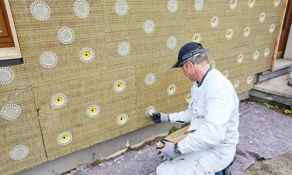 Mann befestigt Tellerdübel in Mineralwolle-Dämmplatten für eine Fassadenisolierung.