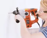 Frau bohrt mit Schlagbohrmaschine ein Loch in die Wand. Sie trägt Schutzbrille.