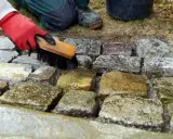 Rote Handschuhe bürsten feuchte Pflastersteine, um sie zu reinigen.