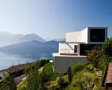 Modernes Haus in Hanglage mit Blick auf einen See und Berge. Ein traditionelles Haus liegt tiefer am Hang.