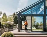 Frau betritt modernen Wintergarten mit Glasdach. Perfekt, um den Sommer zu verlängern und den **Wintergarten planen**.