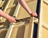 Holzfaserplatte Fassade: Hände sägen Holz für den Hausbau.