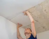 Frau klebt weiße Styropor Deckenplatten an eine alte Decke.
