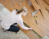 Frau verlegt Laminat, achtet auf die Ausrichtung. Werkzeug liegt bereit. Vermeiden Sie Fehler beim Laminat verlegen.