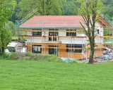 Ein Haus im Bau, umgeben von Gerüsten. Man sieht, wie man ein Haus baut, mit Holzfassade und rotem Ziegeldach.