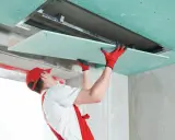 Handwerker mit roten Handschuhen montiert Gipskartonplatten an der Decke, um das Zimmer zu isolieren.