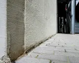 Die Ecke eines Gebäudes wird mit WDVS verputzt. Der Putz ist rau und hellgrau, mit sichtbaren Spuren der Verarbeitung.
