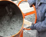 Person in Arbeitskleidung bedient eine Betonmischmaschine, um Beton zu mischen.