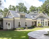 Ein schönes Haus im amerikanischen Stil mit grauer Schindelfassade, großen Fenstern und einem gepflegten Garten mit Pool.