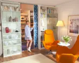 Frau steht vor einem begehbaren Kleiderschrank, den sie selber machen könnte. Links ein Regal mit Geschirr, rechts ein Regal mit Büchern.