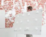 Mann hält Gipskartonplatten mit Klebepunkten, um sie auf unebener Wand zu befestigen.