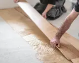 Handwerker verlegen sorgfältig Parkett. Kleber wird auf den Boden aufgetragen, bevor die Holzplanken präzise platziert werden.