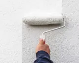 Hand rollt weiße Farbe auf eine strukturierte Wand. Man sieht, welche Wandfarbe am besten deckt.