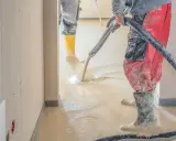 Arbeiter verlegen Estrich mit einer Pumpe. Der flüssige Estrich fließt auf den Boden und wird verteilt.
