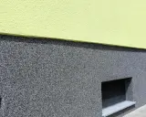 Der Sockel ist mit einem robusten, grauen Körnchenputz verputzt, der gut zu den kleinen Kellerfenstern passt.
