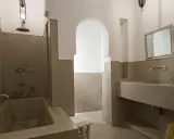 Modernes Badezimmer mit einer freistehenden Badewanne und einem Waschbecken aus Tadelakt. Ein großer Spiegel und ein traditioneller Korb vervollständigen den Look.