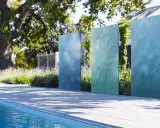 Ausgefallener Sichtschutz Garten selber machen: Vertikale, blaue und grüne Metallplatten vor üppiger Bepflanzung und Pool.