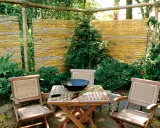 Ein lauschiger Sitzplatz mit einem selbstgemachten Zaun aus Bambus. Holzmöbel und üppige Pflanzen schaffen eine natürliche Atmosphäre.