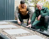 Zwei Männer arbeiten an einer neuen kies terrasse mit quadratischen Trittsteinen.