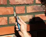 Hand mit Kelle bessert Zementfugen einer Ziegelwand aus.