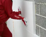 Hand mit Handschuh drückt WDVS Schaum an eine Betonwand.
